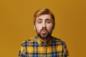 Portrait of fashionable male keeps lips round, wears plaid yellow shirt, isolated over yellow...