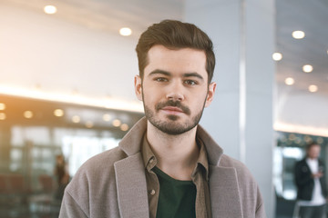 Portrait of outgoing bearded man watching at camera while locating indoor. Journey concept