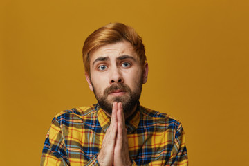 Obraz premium Portrait of serious young bearded male, keep his palms together, prays for good luck on exams. Isolated over yellow background.