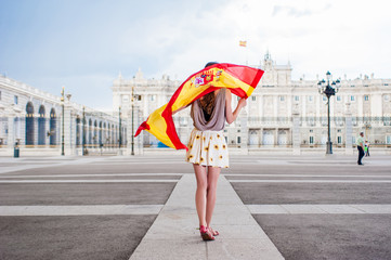 Young woman in front of Palacio de Oriente - the Royal Palace of Madrid, holding a flag with a big smile.