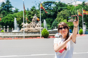 Young tourist woman taking picture with Cibeles Fountain, one of the most famous monuments of architecture of Madrid located on the Cibeles square in the Centre of Madrid, Spain