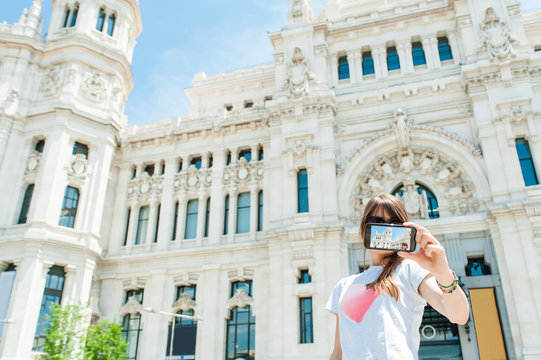 Young tourist woman taking picture in front of Palacio de Comunicaciones located on the Cibeles square in the Centre of Madrid, Spain