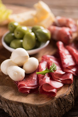 Assorted deli meats and a plate of cheese, on a wooden cutting board. Italian antipasti