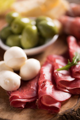 Assorted deli meats and a plate of cheese, on a wooden cutting board. Italian antipasti