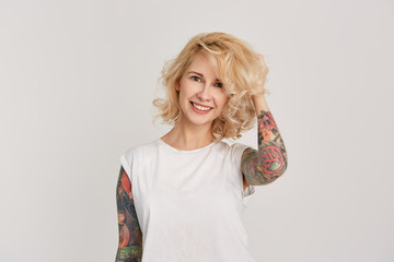 Portrait of young attractive girl wears casual white t-shirt touching her hair. Has tattoos over...