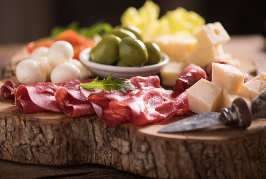 Assorted deli meats and a plate of cheese, on a wooden cutting board. Italian antipasti