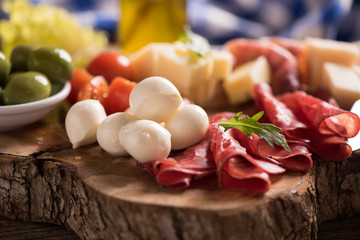 Assorted deli meats and a plate of cheese, on a wooden cutting board. Italian antipasti