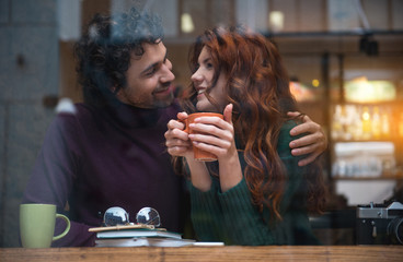 Joyful young lovers dating in cozy cafeteria. They are looking at each other with affection and...
