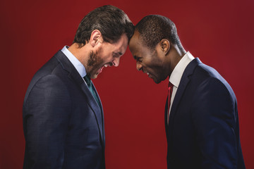 Side view profile of angry young colleagues are fighting each other with foreheads together,...