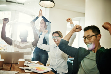 Diverse group of coworkers cheering excitedly in an office meeting