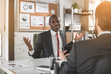 Under negotiation. Portrait of professional young african businessman in suit is sitting at table...