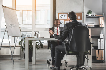 Successful negotiation. Optimistic young qualified african businessman is looking at his skilled partner with smile while sitting at table and having pleasant communication. Copy space