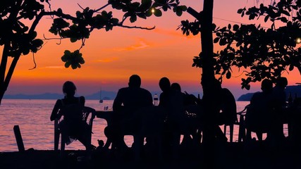 Peoples silhouettes in the tropical beach cafe at sunset