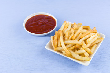 crispy french fries in a ceramic plate served with ketchup on light blue wooden background.