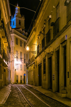Night view of a narrow street in Lisbon, with tram tracks through the Alfama neighborhood