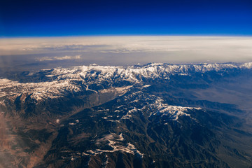 view from the window of the plane on the mountains with snowy peaks and blue clouds