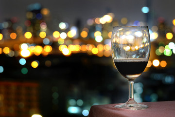 Red Wine Glass Placed on a table overlooking the hotel's backlight. Colorful city lights bokeh background.