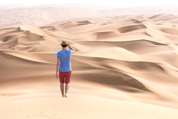 Young causasian male tourist in shorts hiking in giant Liwa desert dunes. Abu Dhabi, UAE.