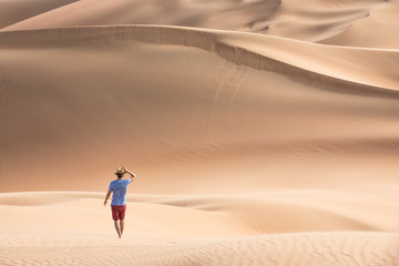 Fototapeta na wymiar Young causasian male tourist in shorts hiking in giant Liwa desert dunes. Abu Dhabi, UAE.