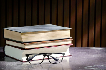 Close-up of reading glasses and old books on the table.