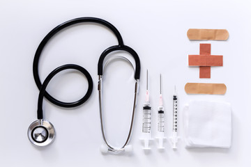 syringe, stethoscope, adhesive bandages and medical gauze bandage on a white table.