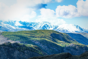 Fototapeta premium Mountain range with snow-covered peaks under the clouds. Landscape of mountain valleys and cliffs.