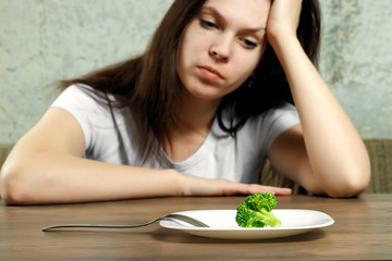 Obraz na płótnie Canvas sad young brunette woman dealing with anorexia nervosa or bulimia having small green vegetable on plate. Dieting problems, eating disorder.