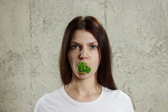 Portrait of a young, beautiful girl holding a broccoli in her mouth.. The concept of a healthy diet, detox, weight loss, diet, eating problems, anorexia, bulimia.