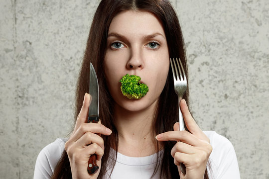 Portrait of a young, beautiful girl holding a broccoli in her mouth.. The concept of a healthy diet, detox, weight loss, diet, eating problems, anorexia, bulimia.