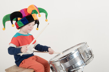 Happy Caucasian child drummer in a carnivalous fool's cap plays on a new drum set. Parents bought the boy a drum for training. Kid in bright clothes with new sticks in his hands be happy at home