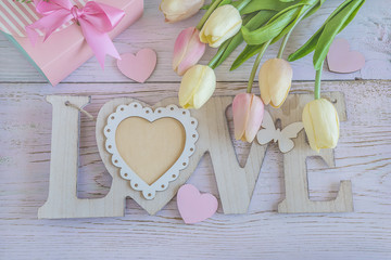 Holiday comporsition with pink gift box, tulips, letters "love" on white colored wooden background