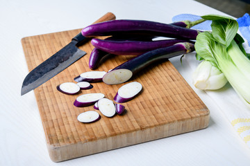 japanese eggplant on wooden board with knife and pak choi salad