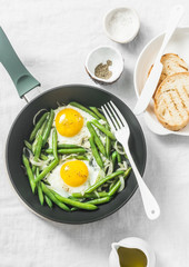 Healthy breakfast or snack - a fried egg with green beans in the cooking skillet on a light background, top view