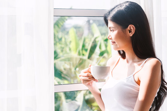 Woman drinking coffee in bedroom in the morning