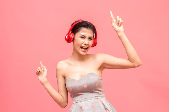 Happy woman with headphones listening to music having fun and dancing on pink background