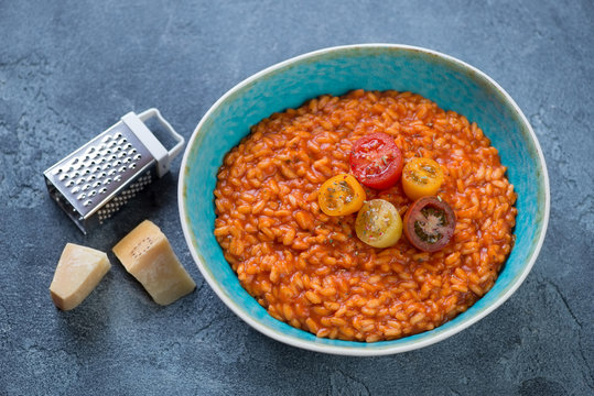 Plate with tomato risotto and parmesan cheese on a blue stone background, studio shot
