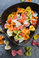 Multicolored farfalle served with salmon slices and cheese in a black plate, vertical shot, close-up