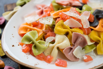 Closeup of boiled multicolored farfalle with salmon slices and parmesan, selective focus