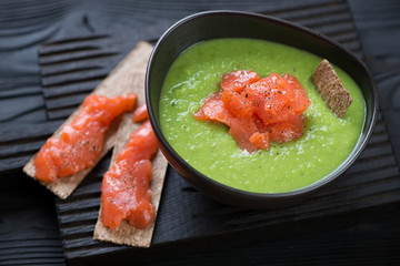 Bowl of green peas cream-soup with addition of salmon on a black wooden serving board, studio shot