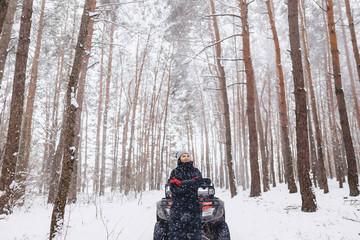 Fototapeta na wymiar young girl on a motorcycle rides in snow-covered pine forest in winter