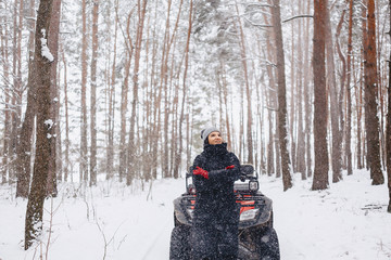 young girl on a motorcycle rides in snow-covered pine forest in winter