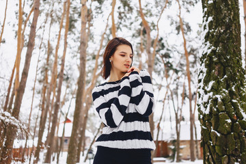 young girl in black and white sweater in the cold at the forest under the pines