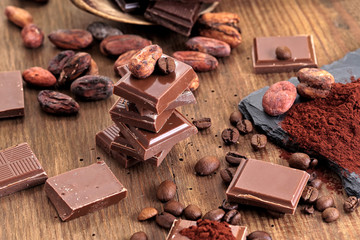 Broken dark chocolate, cocoa powder and coffee beans on a wooden table