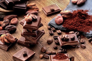 Broken dark chocolate, cocoa powder and coffee beans on a wooden table