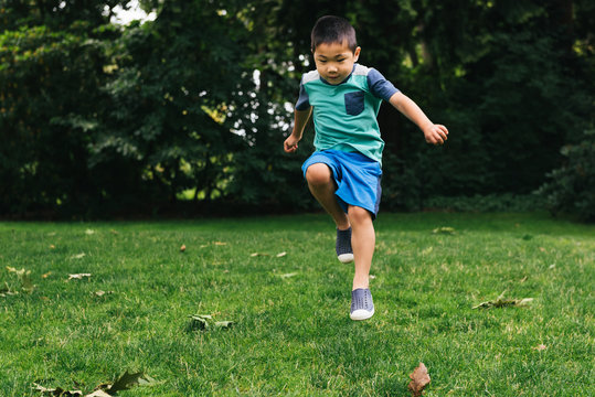 Asian American preschooler skipping in grass at park