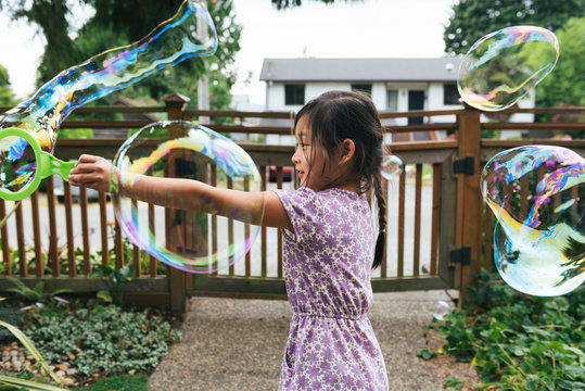 Asian American girl making bubbles outside with bubble wand