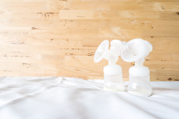 Bottles of automatic breast pump with fresh mother breast milk for baby on white bed sheet and wooden background in bedroom.