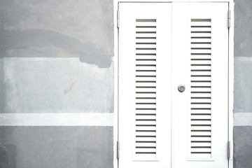 Closed and locked white entrance door on grey painted cement wall background.