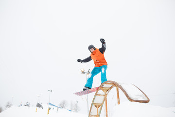 Image of young sportive man skiing on snowboard with springboard against snowy sky