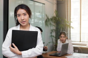 Portrait of leadership young Asian business woman standing in the office with colleagues in meeting room background.